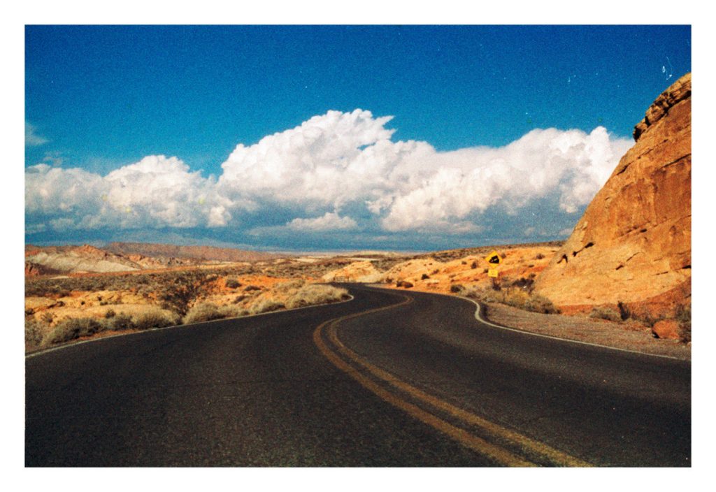 A desert road under a blue sky with clouds.